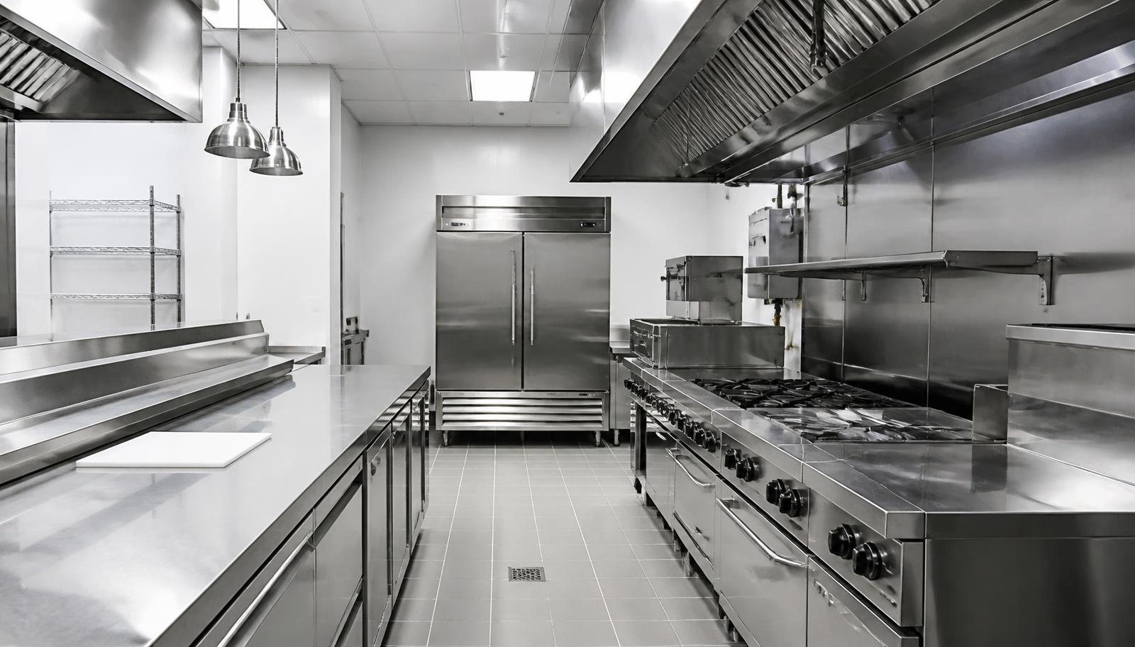 Empty stainless steel commercial restaurant kitchen showing equipment lines, prep counters and hood system